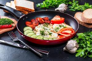Breakfast concept - eggs, sausages, tomatoes and cucumbers in a frying pan