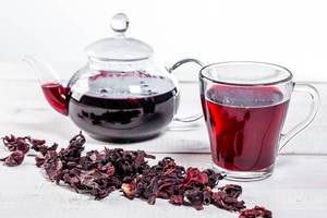 Brewed hibiscus tea in a glass teapot and a Cup with dry hibiscus flowers