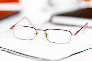 Brille mit dünnem Metallgestell liegt auf Notizheft – fotografiert mit Schärfentiefe