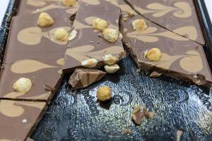 Broken Caramel chocolate with pattern and whole hazelnuts, on a dark tray