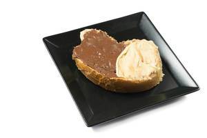 Brotscheibe mit dunkler und weißem Schokoladenaufstrich auf schwarzem eckigem Teller vor weissem Hintergrund