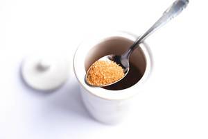 Brown sugar on a metal spoon in a pot on white background
