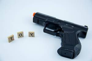 Buchstaben auf Holzquadraten bilden das Wort TOY neben Spielzeugwaffe auf weißem Hintergrund