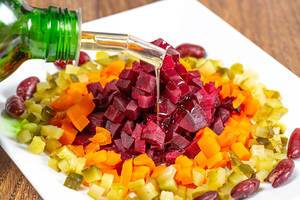 Bunter vegetarischer Salat aus Bohnen, Essiggurken, Karotten und Rote Bete wird mit Öl gegossen
