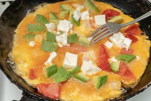 Buntes Frühstück: Omelett mit Avocado, Käse und Tomaten in einer Pfanne