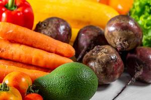 Buntes Obst und Gemüse wie Avocado, Karotten und gelbe Zucchini auf einem weißen Küchentisch