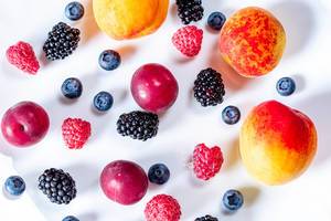 Buntes Obst wie Maulbeeren, Heidelbeeren,  Himbeere,  Pflaume und Aprikosen liegen auf einem weißen Hintergrund