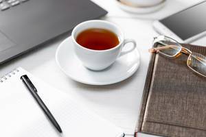 Büroszene mit Laptop und Smartphone, Buch, Notizheft, Schreiber, Brille und einer Tasse Tee