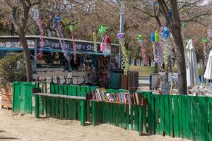 Café Gamar und öffentliche Mini-Bibliothek an einem grünen Zaun, unter Girlanden-Deko aus Plastikmüll im Barceloneta Park in Barcelona, Spanien