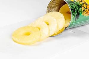 Canned pineapple rings on a white background with a jar