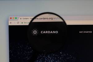 Cardano-Logo am PC-Monitor, durch eine Lupe fotografiert