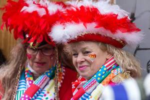Carnival in Germany: woman with colorful costume, red-white feather hat and heart-shaped cologne coat of arms