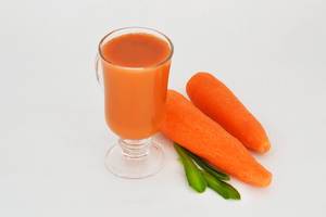 Carrot Juice in a Glass next to two Carrots on white Background