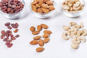 Cashews, almonds and raisins in glass bowls and scattered on a white wooden background (Flip 2019)
