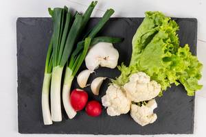 Cauliflower Young Onions Garlic Red Radishes and Lettuce on the black tray