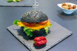 Cheeseburger mit schwarzem Burgerbrot auf einem Steinteller serviert