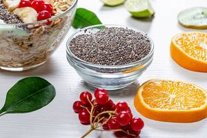 Chia seeds, fresh viburnum, sliced fruit and a bowl of oatmeal on a white wooden background (Flip 2019)