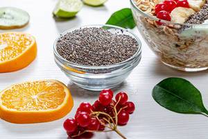 Chia seeds, fresh viburnum, sliced fruit and a bowl of oatmeal on a white wooden background