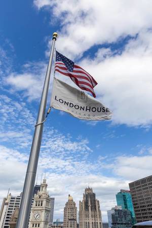 Chicago, "the Windy City": American flag and flag of luxury hotel Londonhouse Chicago blowing in the wind against a backdrop of clouds and high-rise buildings