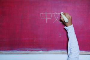 Child writes Chinese word with Chinese simplified characters on chalkboard, learning foreign language