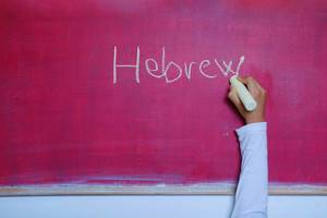 Child writes Hebrew word on chalkboard, learning foreign language