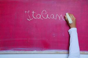 Child writes Italian word on chalkboard, learning foreign language