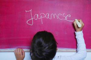 Child writes Japanese word on chalkboard, learning foreign language