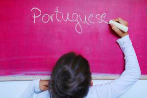 Child writes Portuguese word on chalkboard, learning foreign language