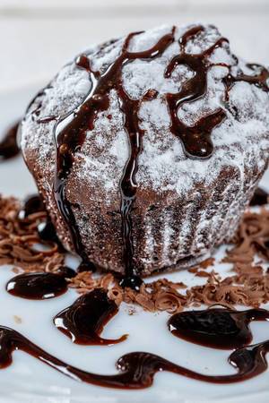 Chocolate muffin with powdered sugar poured chocolate topping