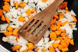 Chopped Carrots and Onions in the frying pan with wooden spoon