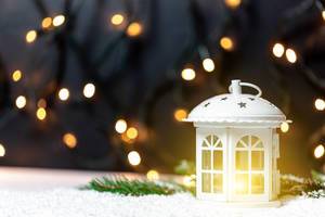 Christmas decoration: a white lantern placed on artificial snow with bokeh lights in the background