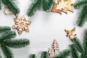 Christmas frame from wooden decorations and Christmas tree branches on a white wooden background