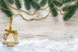 Christmas tree branches, snow and golden Christmas decor on wooden background