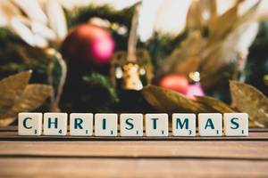 CHRISTMAS written in Scrabble letters on wood with holiday themed background