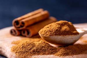 Close Up Bokeh Photo of Cinnamon Powder in a Wooden Spoon with Cinnamon Sticks in the Background