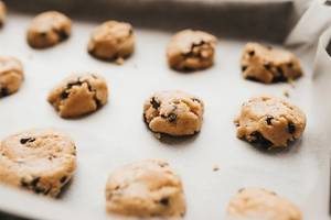Close Up Bokeh Photo of Raw Cookie Dough with Chocolate Chips forming small Cookies on Baking Tray with Baking Paper