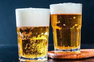 Close Up Bokeh Photo of Two Glasses of Beer with Foamy Top Layer on Dark Background