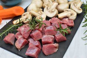 Close Up Cooking Photo of Beef in Cubes with Mushrooms cut in half and Carrots on a Cutting Board