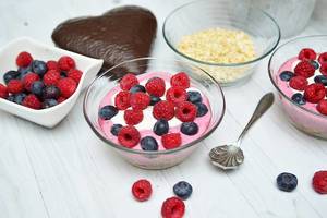 Close Up Food Photo of Bowls with Oatmeal, Yogurt, Raspberries and Blueberries on Wooden Table