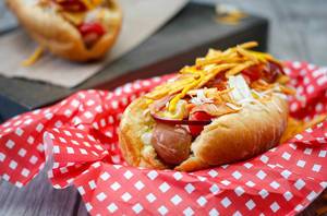 Close Up Food Photo of Hot Dog with crunchy Bacon, Cheddar Cheese, Chips, Cherry Tomatoes, Fresh Onions and Mustard