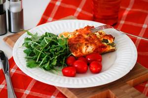 Close Up Food Photo of Quiche with Arugula Salad and Cherry Tomatoes on a White Plate with Fork and Knife