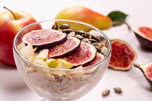 Close-up glass bowl of oatmeal with pieces of figs, pears, yogurt and pumpkin seeds
