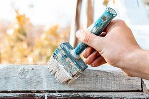 Close up of a brush with white paint in the hand of a man