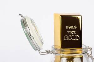 Close up of a gold bar in a glass jar on a white background