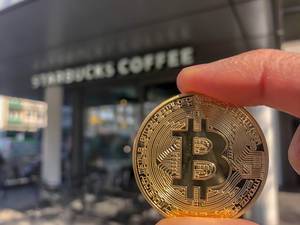 Close-up of a golden Bitcoin in front of Starbucks Coffee at Friesenplatz-Cologne, where you can pay wit cryptocurrency