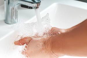 Close up of a man washing his hands and water is pouring from a faucet with spray