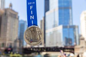 Close-up of a medal with blue ribbon marking the completion of the 2019 Chicago Marathon, with skyscrapers in the background