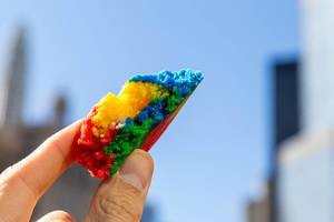 Close-up of a piece of colorful rainbow cookie held between two fingers