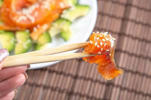 Close-up of a piece of smoked salmon with sesame seeds on chopsticks