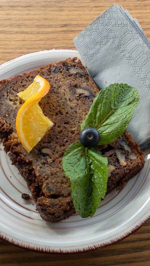 Close-up of a slice of banana bread, garnished with mint leaves and an orange slice